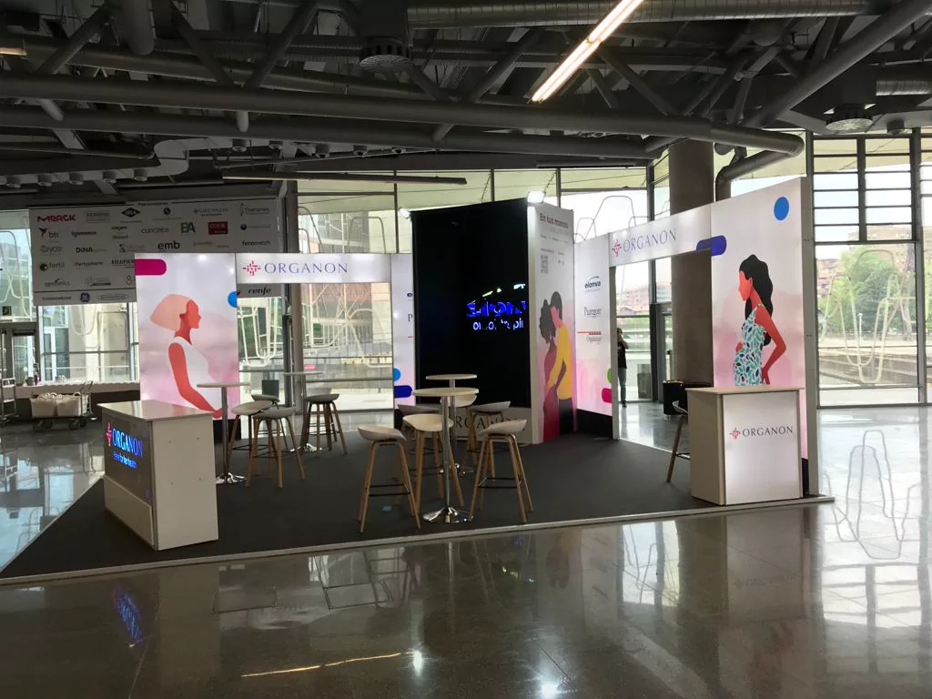 Stand abierto de Organon con paneles ilustrados, mostradores iluminados y zona de reuniones