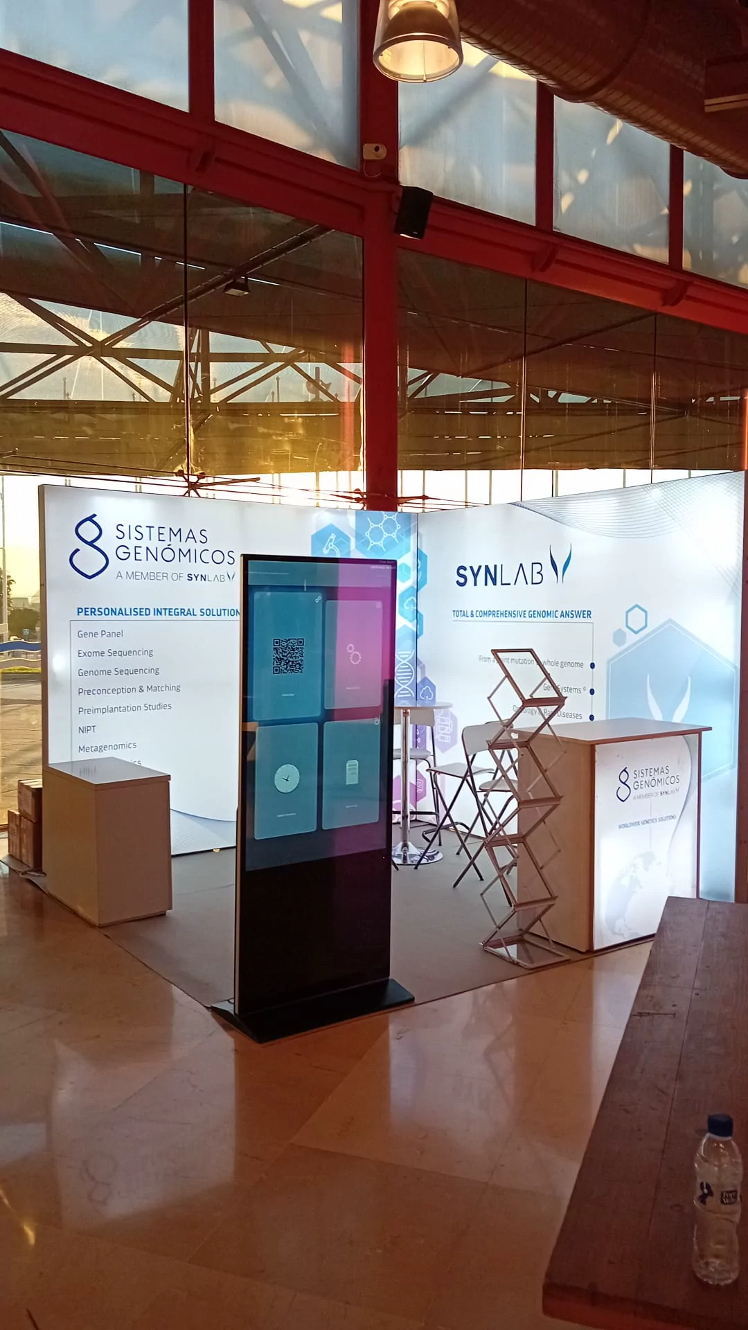 Stand vertical de Sistemas Genómicos y Synlab con tótem digital y gráfica iluminada